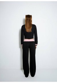 Czarna krótka kurtka z długimi rękawami i różowym pasem, zestawiona z czarnymi spodniami o szerokich nogawkach. Gładka tekstura z kontrastującymi różowymi akcentami.