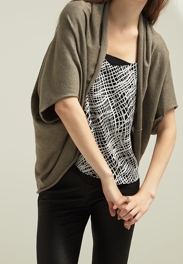 Cárdigan verde oliva con corte holgado, textura suave y diseño drapeado. Debajo, una blusa con motivo de cuadrícula en blanco y negro combinada con pantalones negros.