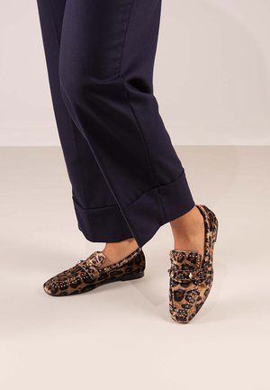 Mocasines de estampado de leopardo con suela plana y detalles decorativos de hebilla, hechos de material suave, combinados con pantalones azul marino.