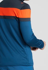 Maglietta atletica a maniche lunghe blu con strisce orizzontali arancioni e blu navy nella parte superiore, realizzata in materiale liscio ed elastico.