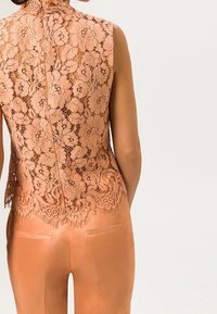 Lace-back top i blød ferskenfarve med blomsterprint, høj krave og scalloped kant; parret med glatte, tætsiddende ferskenbukser.
