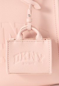 Light pink leather bag with a textured surface, featuring a small attached tag with embossed "DKNY" branding and a rounded handle.