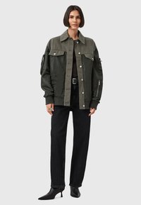 Giacca verde a più trame con design colletto, hardware argentato, maniche voluminose e tasche laterali, abbinata a jeans neri e stivaletti a punta.
