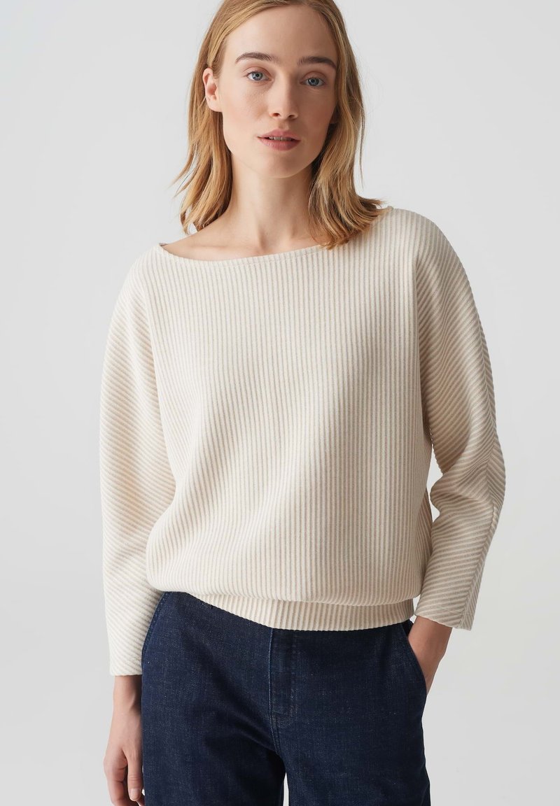 Pullover a righe beige con ampio scollo a barca e maniche lunghe. Caratterizzato da una vestibilità comoda e texture a costine. Abbinato a pantaloni blu navy.