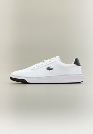 Baskets basses blanches avec semelle noire, languette de talon noire, lacets blancs et logo crocodile Lacoste noir sur le côté.