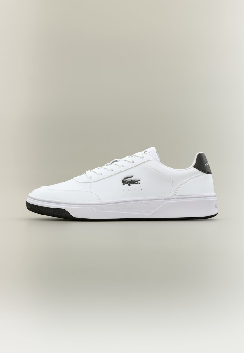 Baskets basses blanches avec semelle noire, languette de talon noire, lacets blancs et logo crocodile Lacoste noir sur le côté.