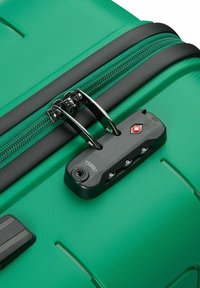 Valigia verde rigida con superficie testurizzata, zip nera e lucchetto approvato dalla TSA. Presenta accenti lisci e maniglie integrate.