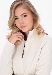 Pullover in pile beige chiaro con colletto alto, zip a quarto e hardware argentato. Presenta una superficie morbida e testurizzata e maniche aderenti.