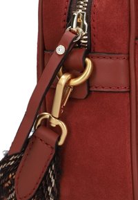 Borsa in suede rosso con hardware dorato, zip e una tracolla decorativa. Presenta un accento testurizzato e dettagli in pelle liscia.