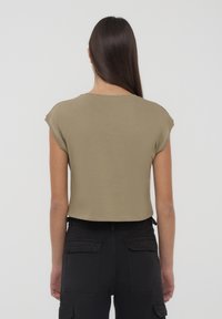 Top corto e a maniche corte in misto cotone verde oliva, con scollo rotondo e una texture liscia. Indossato con pantaloni cargo neri.
