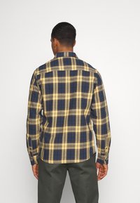 Camisa de cuadros de manga larga con un patrón de cuadros amarillos y marinos, hecha de tela texturizada con puños y cuello abotonados.