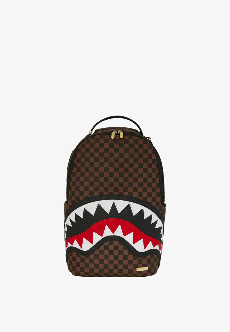 Mochila marrón a cuadros con un gran diseño de boca de tiburón en blanco, rojo y negro. Incluye cremalleras doradas y un asa superior.