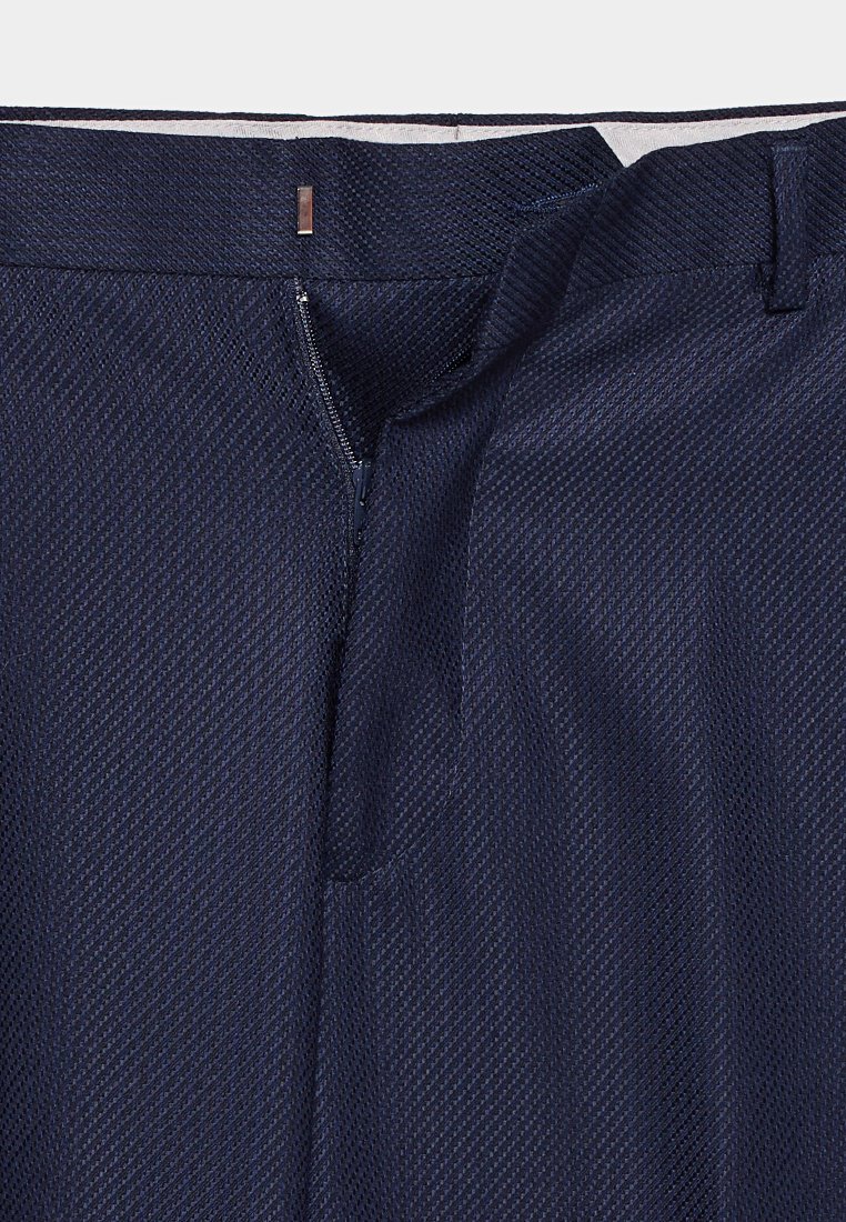 Navyblaue, strukturierte Hose mit teilweise offenem Reißverschluss und einem Bund, der über einen silbernen Verschluss und Gürtelschlaufen verfügt.