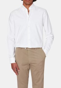 Camicia bianca con colletto classico, realizzata in cotone leggero. Abbinata a pantaloni beige, con tasche laterali e frontale piatto.