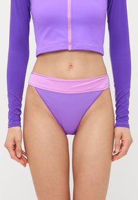 To-delt badetøy med langermet topp og bikini-bunn i forskjellige nyanser av lilla, laget av glatt, elastisk stoff.
