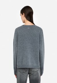 Maglione grigio con una vestibilità rilassata, realizzato in materiale morbido. Presenta un collo rotondo, spalle scese e un piccolo logo sul retro.