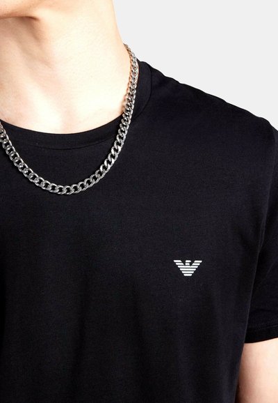 Maglietta nera in cotone con un piccolo logo a strisce bianche sul pettorale sinistro. Accompagnata da una collana a catena spessa in argento.