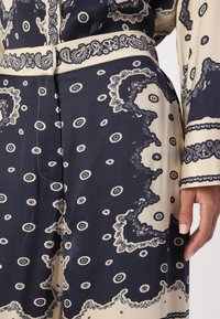 Abito stampato di blu scuro e crema con motivi paisley, maniche lunghe e cintura in vita. Realizzato in tessuto morbido con dettagli elaborati.