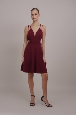 Burgundy dress with a deep V-neck, thin shoulder straps, and side cutouts; A-line skirt, smooth fabric, paired with black strappy heels.