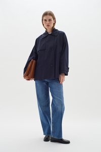 Jūras zila pārmēra jaka ar platu apkakli, divām lielām priekšējām pogām un krūšu kabatu, savienota ar gaiši ziliem džinsu un melniem mokasīniem.