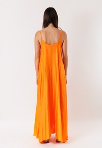 Abito maxi arancione senza maniche con una silhouette ampia, schiena dritta e spacco laterale. Realizzato in tessuto morbido e leggero.