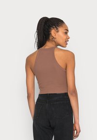Top cropped castanho com design de alças cruzadas, textura canelada e tecido suave, combinado com jeans pretos de cintura alta.