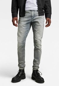 Svetlo sivi ozki jeans z izpiranjem, z gumbom in zadrgo ter sprednjimi žepi, kombinirani s črnimi vojaškimi čevlji z vezalkami.