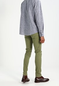 Grå knapp-up skjorta med mönstrad textur, i kombination med olivgröna byxor och bruna läderskor. Fokusera på en avslappnad, ledig passform.