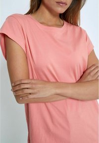 Šviesiai rožinė trumpa rankovė t-shirt su apvaliu iškirpimu. Lygus medvilnės audinys, laisvas šešiakampio kirpimas, šiek tiek suktos rankovės ir be matomų raštų.