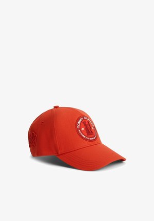 Helles rotes Baseballcap mit gebogenem Schirm, vorne mit rundem Tommy Hilfiger Logo-Patch und geprägtem Design an der Seite.