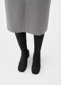 Μαύρες μπότες μέχρι το γόνατο από υλικό με υφή, με μυτερή μύτη και σχεδιασμό με συγκέντρωση υφάσματος. Συνδυασμένες με γκρι ένδυμα μήκους μέχρι το γόνατο.