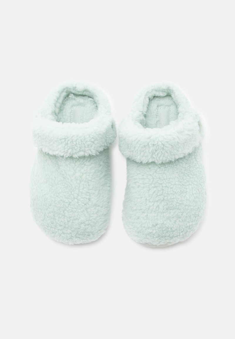 Par de suaves pantuflas de forro polar azul claro con puños doblados, diseñadas para la comodidad y el calor en interiores, exhibidas sobre un fondo blanco liso.