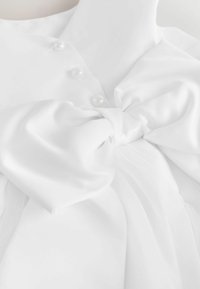 Weißes Satin-Kleid auf einer Schaufensterpuppe mit großer gebundenen Schleife an der Taille und drei Perlenknöpfen am Oberteil.