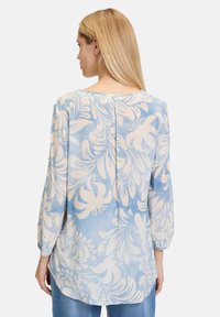 Blusa azzurro chiaro con un motivo floreale bianco, maniche lunghe e dettaglio con plissé sulla schiena. Tessuto morbido con una vestibilità comoda.