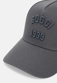 Pilkas beisbolo kepurė su iškiliais "BOGGI" ir "1939" užrašais priekyje, pagaminta iš tekstūruotos medžiagos su kreivu slėniu.