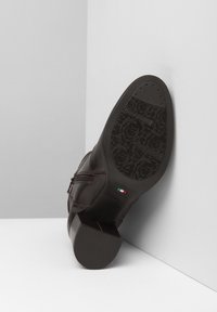 Zapato de cuero marrón con un tacón bajo, que presenta una suela de goma texturizada y una cremallera lateral. El interior muestra las marcas de la marca y una etiqueta de hecho en Italia.