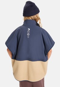 Marine buitensponcho met een beige fleece onderkant, hoge kraag en een logo graphic op de achterkant. Beschikt over brede mouwen en een golvende zoom.