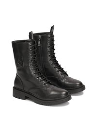 Botas de cuero negro hasta el tobillo con puntera redondeada, cierre de cremallera, cordones delanteros y suela de goma texturizada. Presentan un logo grabado en el lateral.