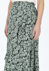 Jupe florale présentant un fond noir avec des fleurs vert clair, fabriquée à partir d'un tissu léger, avec des plis et une taille ajustée.