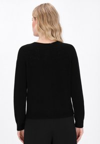 Zwarte gebreide trui met lange mouwen, een ronde hals en textuurdetails op de achterkant. Zachte stof met een ontspannen pasvorm.