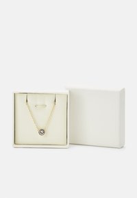 Collier en or avec un pendentif rond mettant en valeur une pierre centrale, présenté dans une boîte blanche avec un intérieur doux.