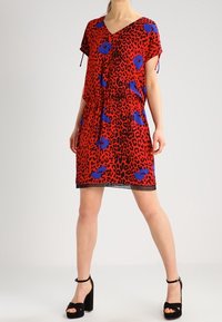 Vestido corto rojo con estampado de leopardo y acentos florales azules. Manga corta, escote en V, cintura ceñida y un detalle decorativo en el dobladillo.