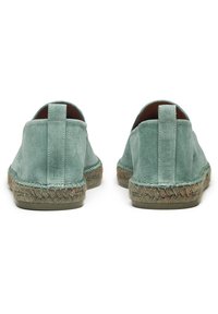 Scarpe slip-on in suede di un leggero verde acqua, con una suola intermedia in giunco intrecciato e una suola esterna in gomma testurizzata. Design minimalista con un occhiello posteriore.
