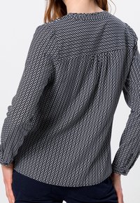 Camicia a righe bianco e nero con un design a onde, maniche lunghe e dettagli arricciati alle spalle e sulla parte posteriore.