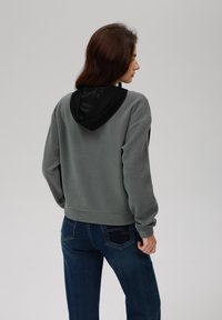 Grå fleecegenser med svart hette, med en cropped design og elastiske mansjetter. Kombinert med mørkeblå jeans som viser lommedetaljer.
