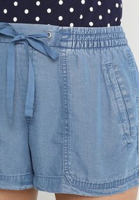 Pantalones cortos de mezclilla azul claro con cintura elástica, cordón ajustable y bolsillos laterales. Textura suave con un ajuste relajado y diseño casual.