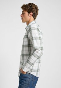 Camicia a maniche lunghe a quadri bianca e verde, con colletto button-down, taschino sul petto e bottoni sui polsini; tessuto misto cotone con una texture liscia.