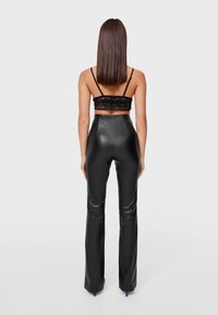 Zwarte nep leren high-waisted flared broek met een gladde textuur en een aansluitende pasvorm, gecombineerd met een zwarte kanten bralette.
