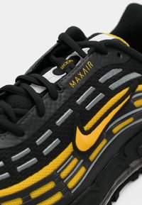 Zwarte en gele sportafdeling met "MAX AIR" merk, reflecterende zilveren accenten en een zichtbare luchtkussenzool.