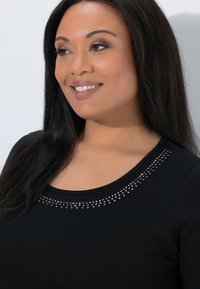 Black shirt featuring a round neckline accented with a row of silver rhinestones along the collar, made from a soft, smooth fabric.